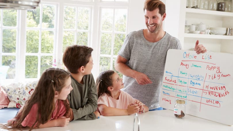 Papá mostrando la lista de la tabla de tareas a sus tres hijos