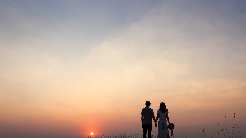 Pareja tomados de la mano viendo el amanecer al aire libre